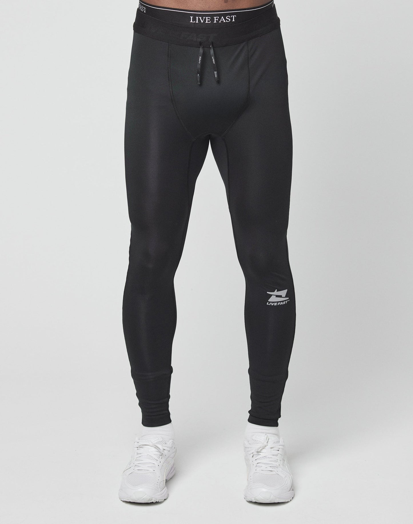 A person wearing Live Fast Performance Tights by LIVE FAST DIE YOUNG, featuring a slim fit and branded waistband, stands against a plain white background paired with white sneakers.