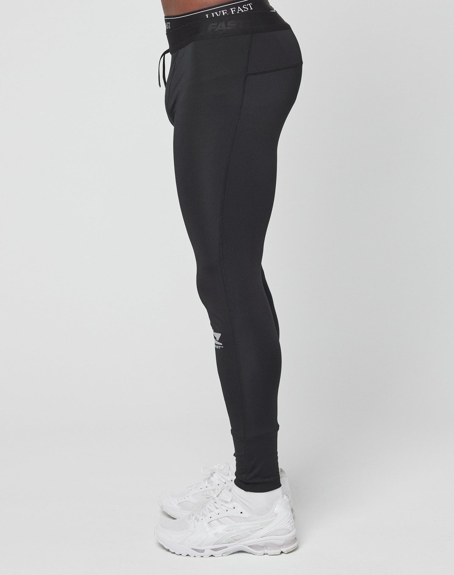 A person in Live Fast Performance Tights by LIVE FAST DIE YOUNG, featuring a Slim Fit and logo near the knee with an Elastikbund drawstring waistband, stands in white sneakers against a plain white background.
