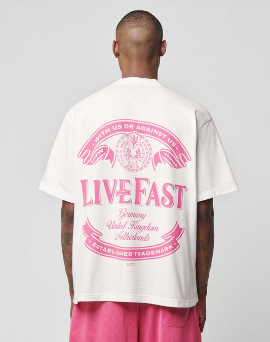 Wearing the LFDY Loyal Tee by LIVE FAST DIE YOUNG, an oversize white Baumwolle shirt with pink front and back print reading LIVE FAST above Germany, United Kingdom, Netherlands, and Established Trademark; paired with pink shorts.