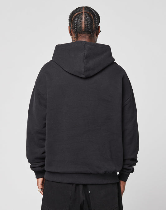 A person with braided hair is seen from behind, wearing the LIVE FAST DIE YOUNG LFDY Script Hooded black oversize sweatshirt (100% Baumwolle) and black pants against a plain light background.