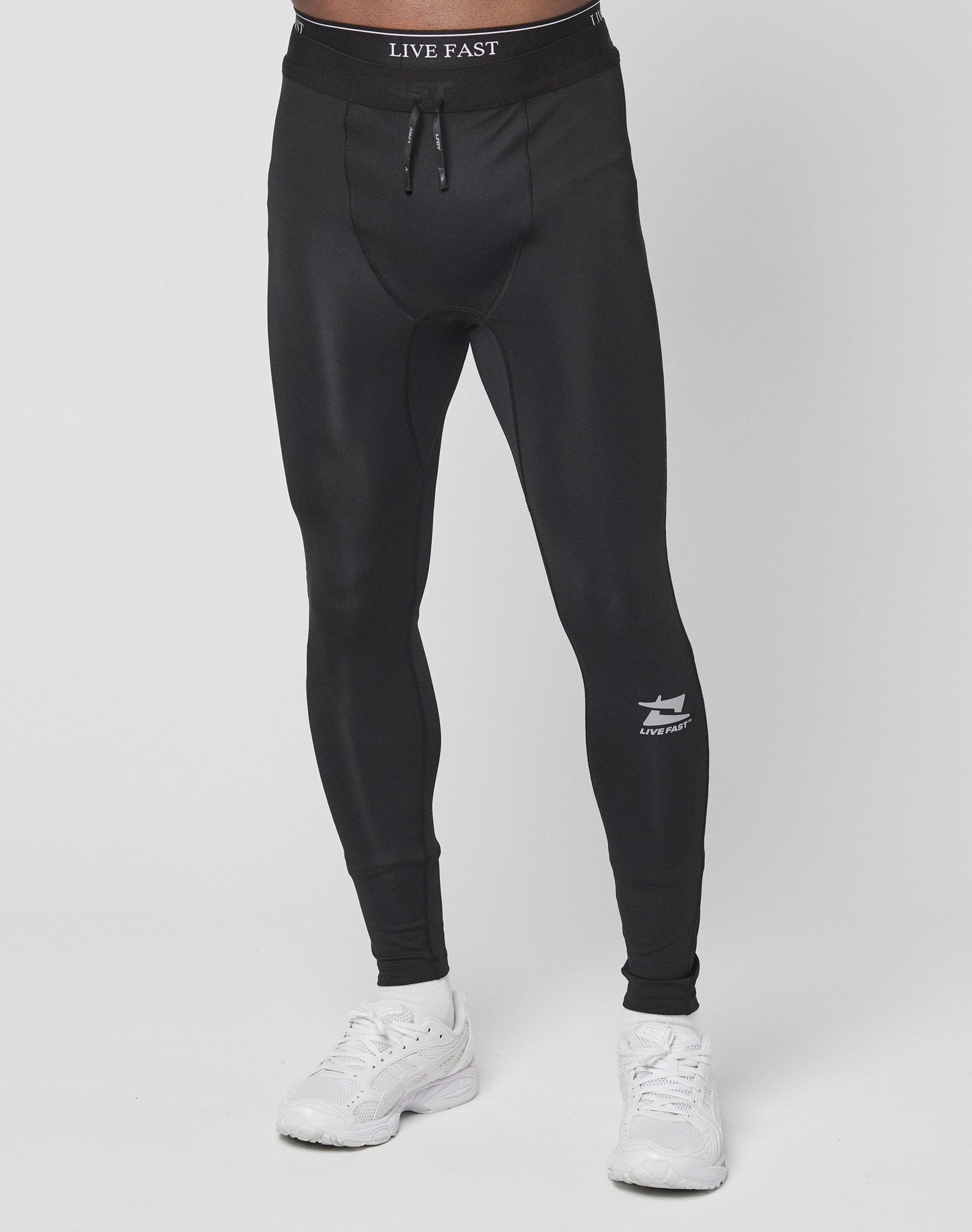 A person wears Live Fast Performance Tights by LIVE FAST DIE YOUNG, featuring a slim fit and branded elastic waistband, paired with white sneakers, standing against a plain white background.