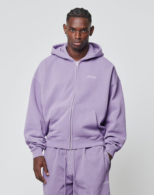 A man faces forward in a matching light purple LIVE FAST DIE YOUNG Basic Script Hooded Zip and sweatpants aus Baumwolle, featuring a small logo embroidery on the left chest. The plain background is light gray.