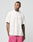 A man wearing a white LFDY Loyal Tee by LIVE FAST DIE YOUNG with an oversize fit and pink shorts stands against a plain light background, looking left with his hands in his pockets.