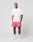 A man stands facing forward in a studio, wearing a white T-shirt and pink LFDY Oval Mesh Shorts by LIVE FAST DIE YOUNG with an elastic waistband. His tattooed arms are relaxed at his sides against a plain light gray background.
