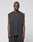 A person faces forward in an oversize fit LFDY Run Club Muscle Shirt by LIVE FAST DIE YOUNG, sleeveless and dark gray with matching pants, made from 100% Baumwolle and featuring a small white chest logo, against a plain light gray background.