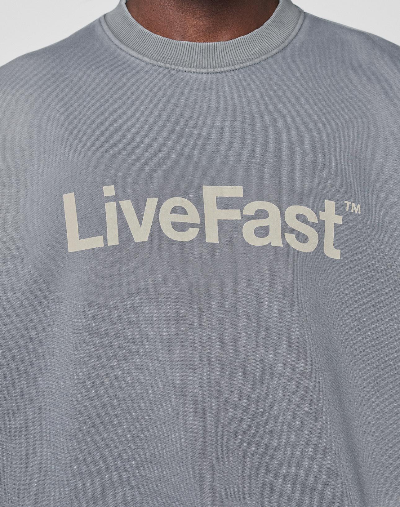 A person wears the Basic LiveFast Sweater by LIVE FAST DIE YOUNG—a gray, oversize-fit sweatshirt with "LiveFast™" in bold, pale letters on the chest and a subtle hand-finished fade effect for a lived-in look.