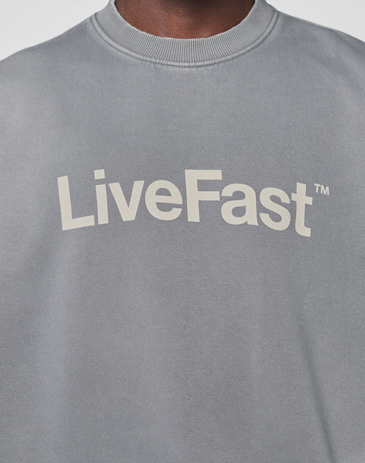 Close-up of the Basic LiveFast Sweater by LIVE FAST DIE YOUNG, a grey sweatshirt with a faded finish and bold white "LiveFast" lettering alongside a small TM symbol.