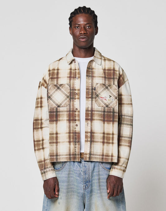 A person faces forward against a plain white background, wearing LIVE FAST DIE YOUNG’s Faded Flannel in beige and brown plaid with two chest pockets and oversize fit, paired with light blue baggy jeans—all made from soft Baumwolle. | model