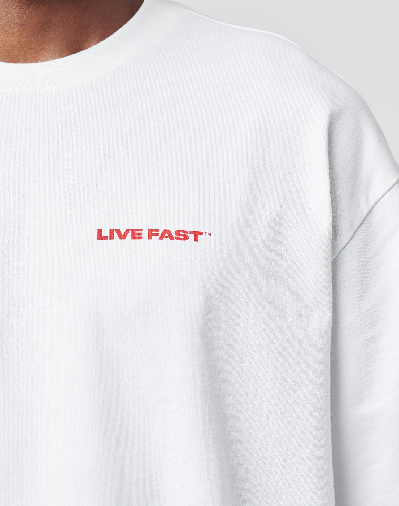 Close-up of a person wearing the LFDY Cinema Tee by LIVE FAST DIE YOUNG—an oversize white sweatshirt with LIVE FAST in bold red on the upper left chest. Crafted from 100% Baumwolle for superior comfort and style.