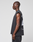 A person stands in profile against a plain background, wearing an oversize fit LIVE FAST DIE YOUNG LFDY Run Club Muscle Shirt—sleeveless and dark gray with large white back graphics—and matching dark pants.
