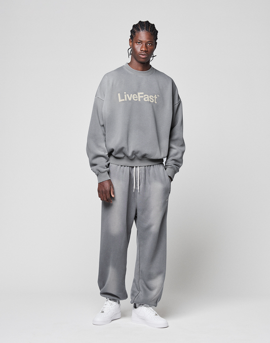 A person stands against a plain background wearing the Basic LiveFast Sweater by LIVE FAST DIE YOUNG, paired with matching grey faded sweatpants and white sneakers.