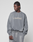 A person in an Oversize Fit grey Basic LiveFast Sweater by LIVE FAST DIE YOUNG and sweatpants looks to the side. The handgefertigter Fade-Effekt and bold LiveFast print stand out against the plain light grey background.