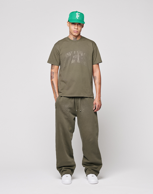 A person stands facing forward wearing the olive green Live Fast Rhinestone Tee by LIVE FAST DIE YOUNG, matching baggy sweatpants, a green baseball cap, and white sneakers against a plain light gray background.