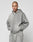 A person with a shaved head and visible tattoos wears the LIVE FAST DIE YOUNG Basic Hooded Zip in light gray with subtle logo print, paired with matching sweatpants, standing against a plain, light background with hands in pockets.
