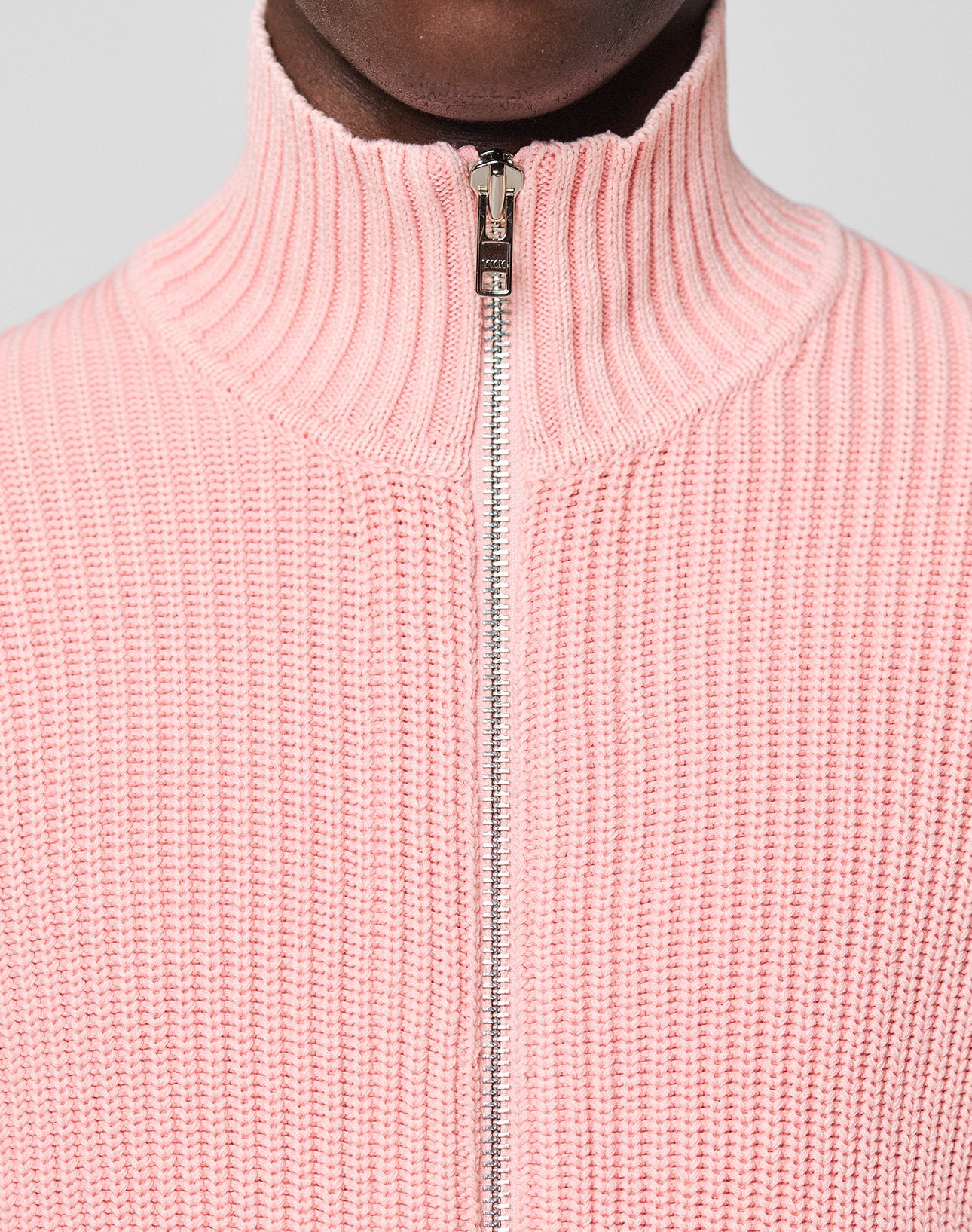 Close-up of a person in the LFDY Knit Jacket by LIVE FAST DIE YOUNG, featuring a light pink ribbed knit, 100% Baumwolle, high Stehkragen, metallic zipper, and soft texture with modern regular fit details in sharp focus.