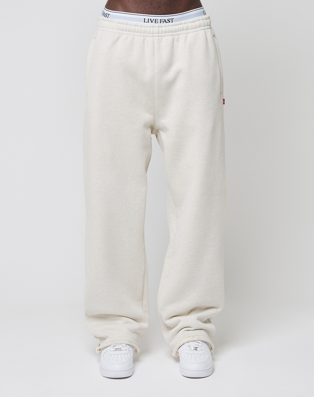 A person wears off-white LFDY Heavyweight Loungepants by LIVE FAST DIE YOUNG with white sneakers. The waistband reveals underwear with LIVE FAST lettering, set against a plain white background.