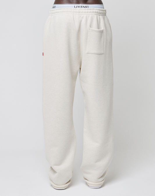 Wearing off-white LFDY Heavyweight Loungepants by LIVE FAST DIE YOUNG, featuring 650gsm soft cotton, a wide fit, high elastic and exposed branded waistband, plus a square patch pocket on the right hip, against a plain white background.