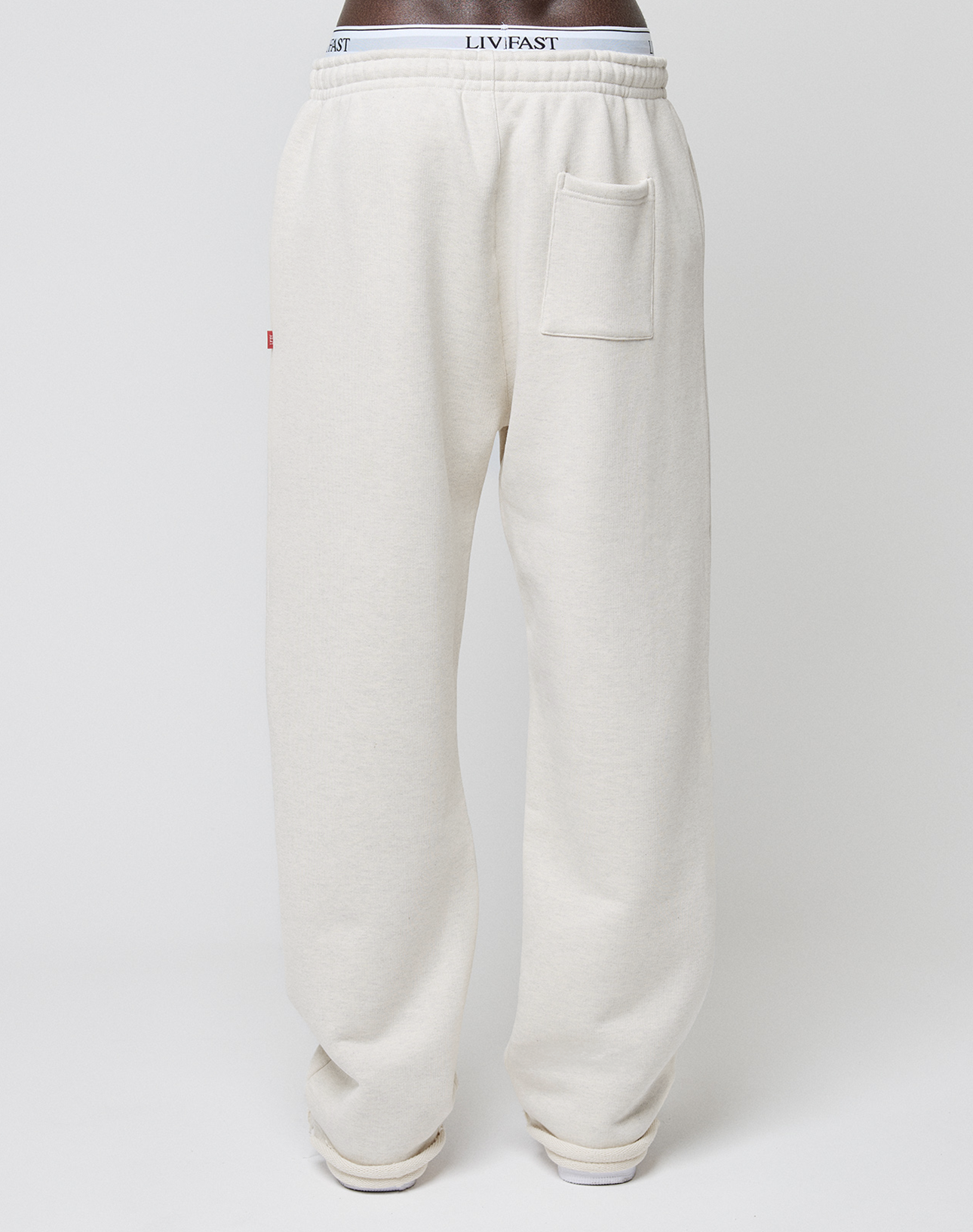 Wearing off-white LFDY Heavyweight Loungepants by LIVE FAST DIE YOUNG, featuring 650gsm soft cotton, a wide fit, high elastic and exposed branded waistband, plus a square patch pocket on the right hip, against a plain white background.