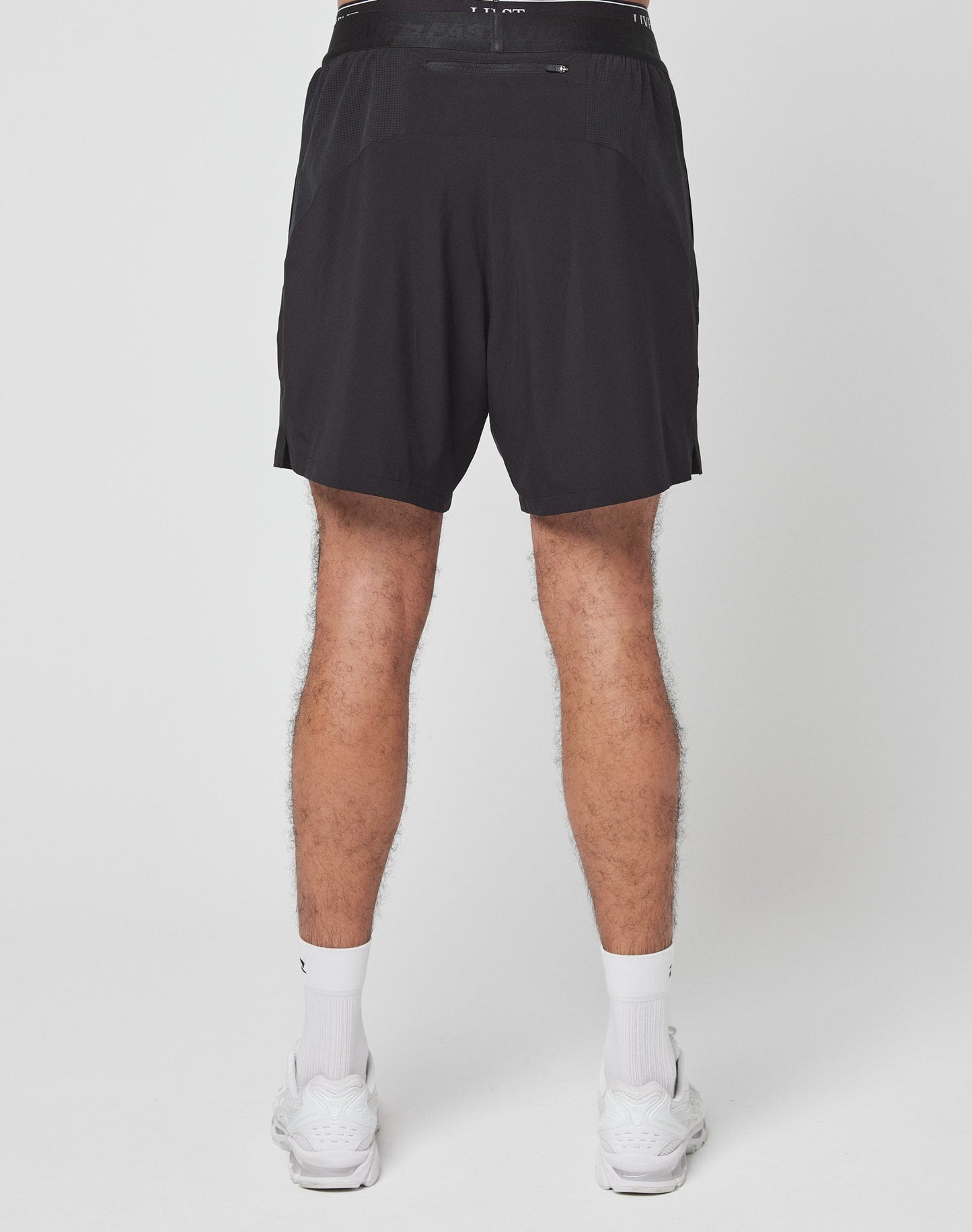 A person stands against a plain white background wearing LIVE FAST DIE YOUNG’s Live Fast Performance Shorts—black with LIVE FAST on the elastic waistband, regular fit—paired with white socks and sneakers. The photo is cropped at the waist and ankles.