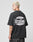 A person with short blond hair, dressed in the LIVE FAST DIE YOUNG LFDY Bulge Tee—an oversized black cotton shirt with a large white Everybody Livefast Eats backprint—stands sideways facing left against a plain light gray background.