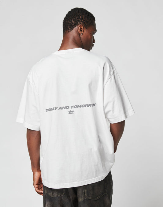 A person faces away from the camera in an oversize LIVE FAST DIE YOUNG LFDY Trinity Tee, made from 100% Baumwolle, featuring TODAY AND TOMORROW in reflective print across the upper back. The background is plain and neutral.