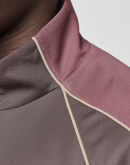 Close-up of a person wearing the LFDY x Baba Angora Trackjacket by LIVE FAST DIE YOUNG, featuring an oversize fit and high collar in mauve and brown with light beige piping. Only the neck and shoulder are visible.