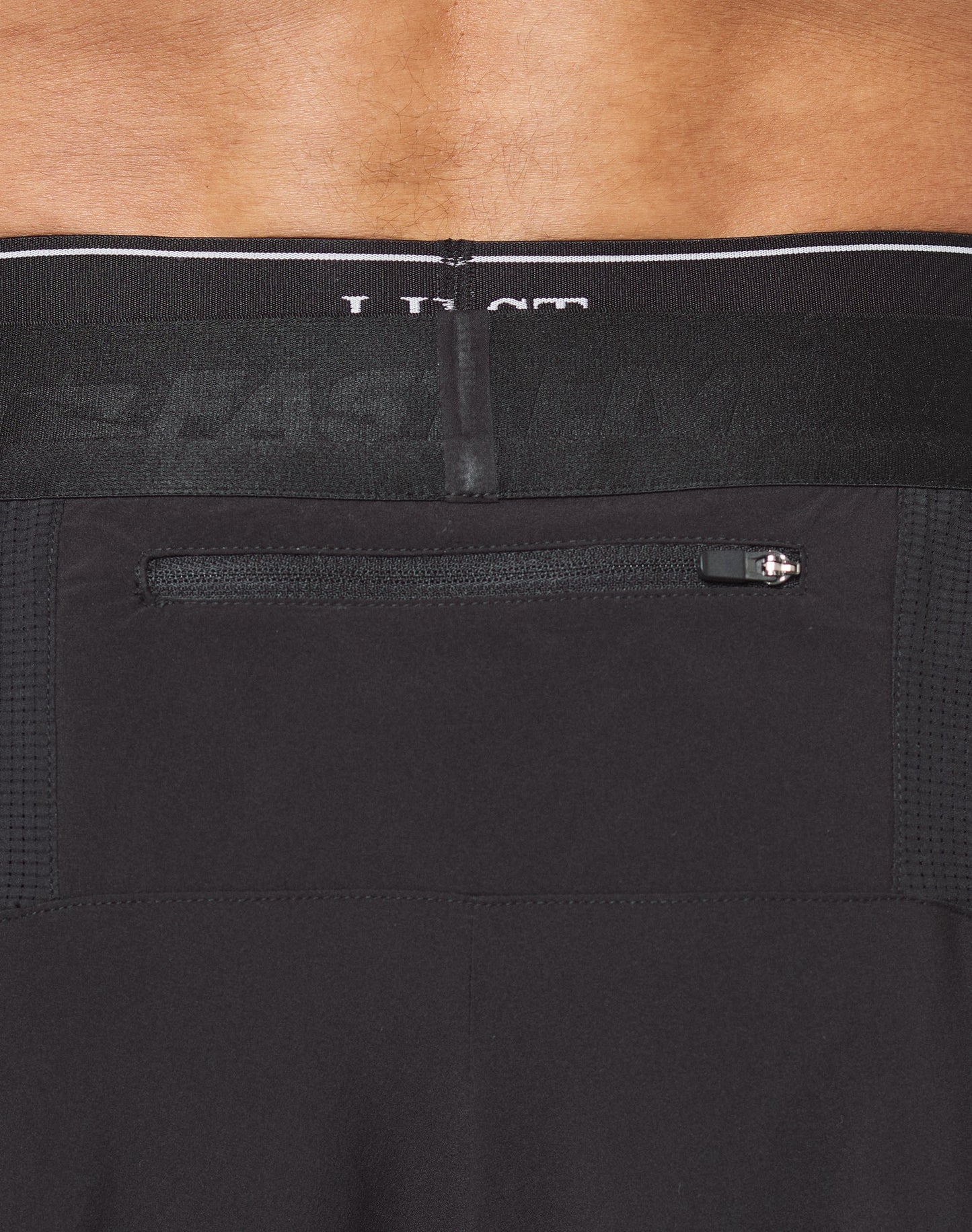 Close-up of a person wearing LIVE FAST DIE YOUNGs Live Fast Performance Shorts. The black Regular Fit shorts feature an elastic waistband, reflective logo print, and LIVE FAST text on the lower left leg.