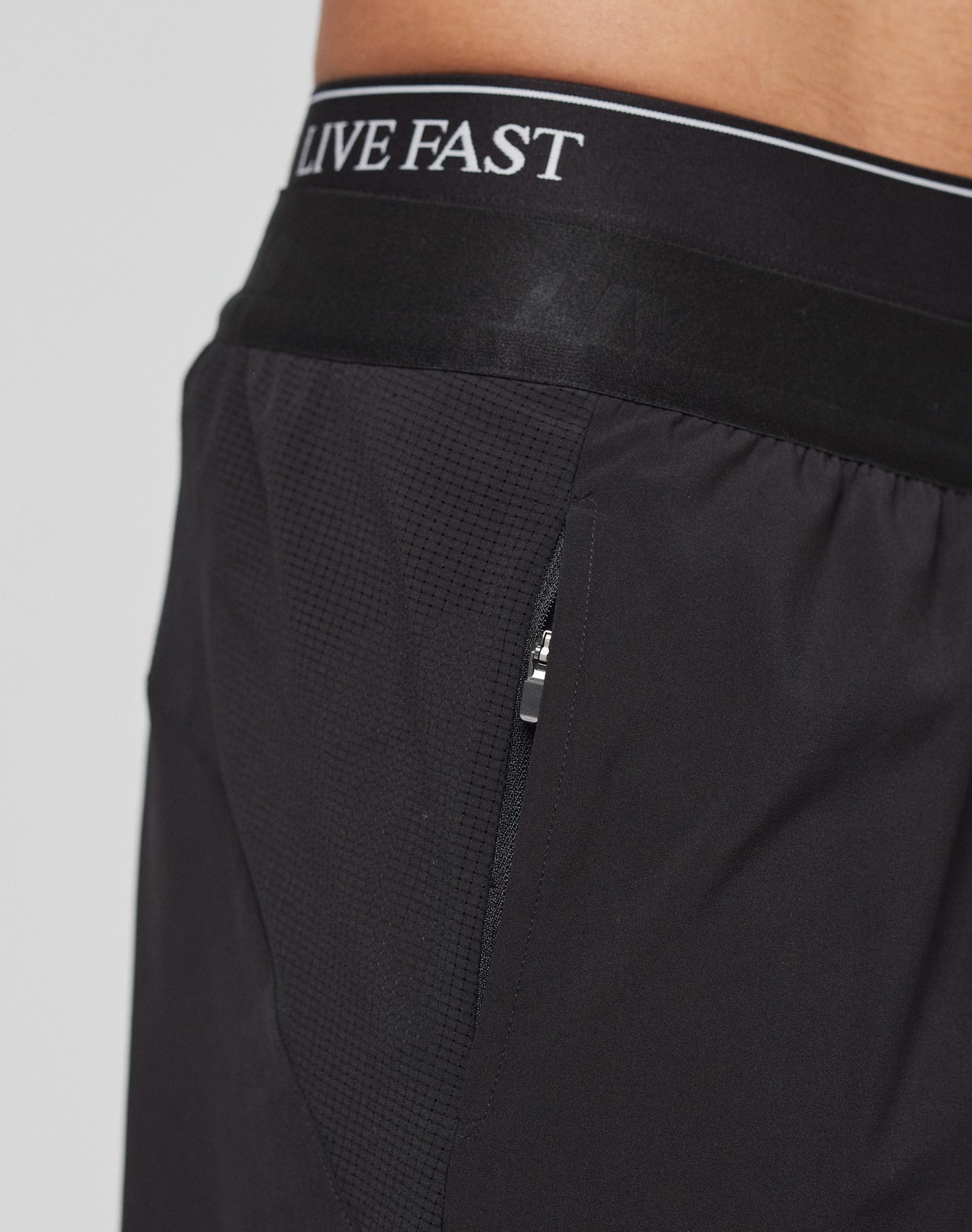 Close-up of a person wearing LIVE FAST DIE YOUNGs Live Fast Performance Shorts, featuring a regular fit, zippered pocket, and an elastic waistband with LIVE FAST in white letters.