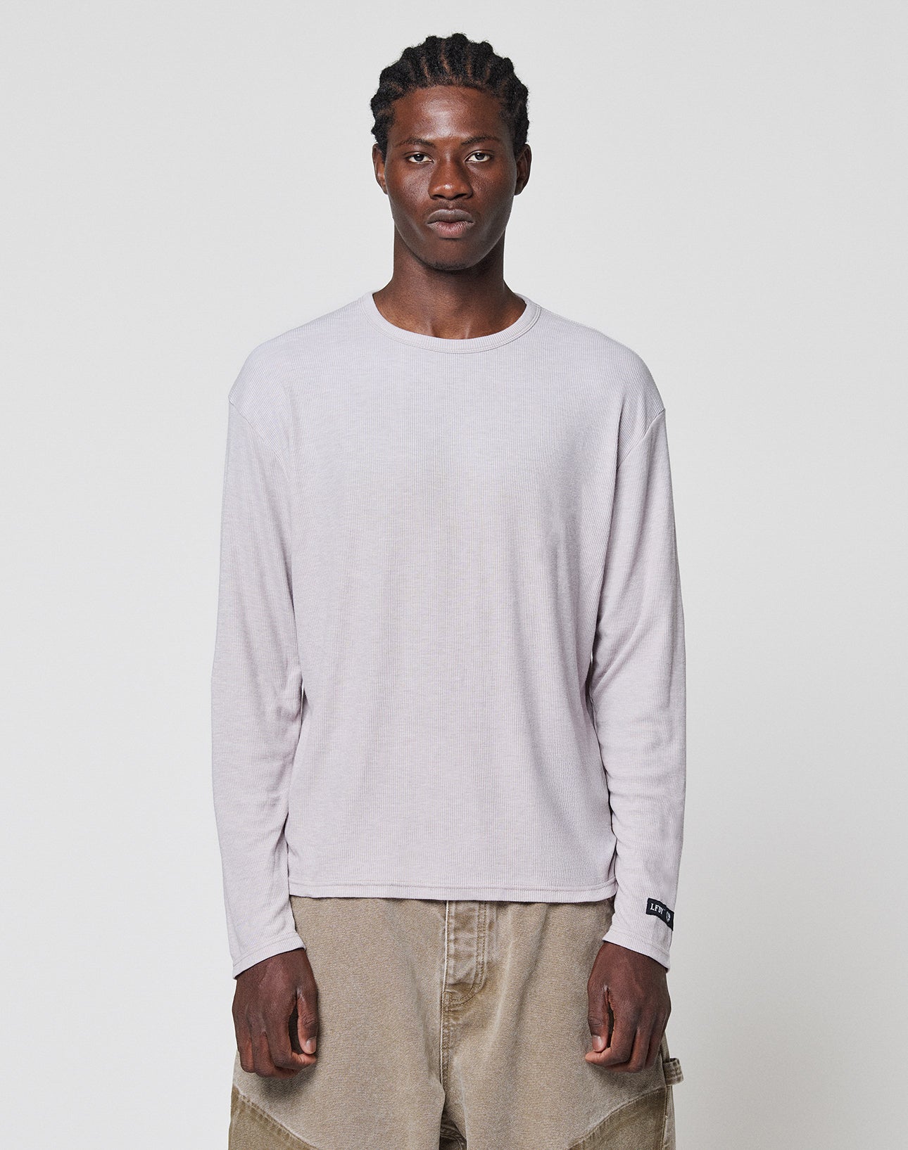 A man with braided hair wears the LIVE FAST DIE YOUNG LFDY Rib Longsleeve and loose tan pants, standing facing forward against a plain white background. | model