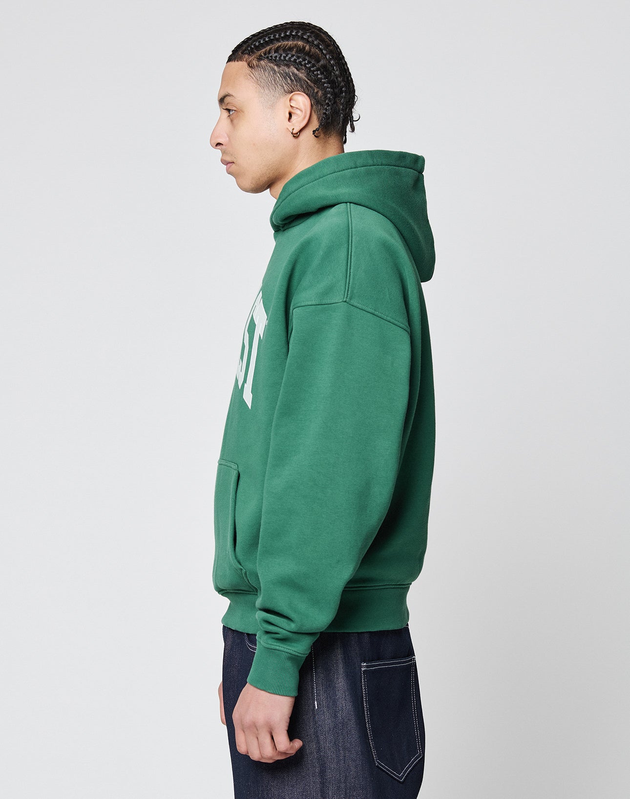 A young person with braided hair stands in profile, wearing the LIVE FAST DIE YOUNG Live Fast College Hooded sweatshirt with white front print and dark jeans against a plain light background.