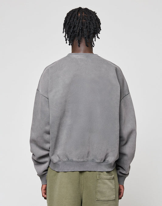 A person with short, twisted hair is shown from the back, wearing a LIVE FAST DIE YOUNG Basic Blank Sweater in gray and olive green pants with a right-side pocket. The background is plain and light-colored.