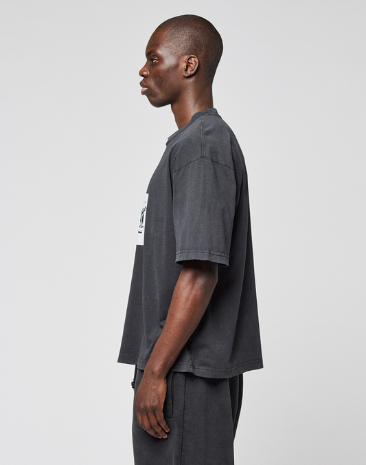 A man in profile against a light background wears the LFDY 40 Tee by LIVE FAST DIE YOUNG, a loose dark gray oversize-fit T-shirt made from 100% Baumwolle, paired with matching pants. His arms are relaxed at his sides as he looks ahead.