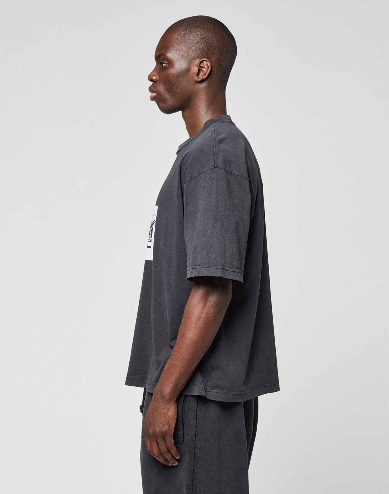 A man in profile against a light background wears the LFDY 40 Tee by LIVE FAST DIE YOUNG, a loose dark gray oversize-fit T-shirt made from 100% Baumwolle, paired with matching pants. His arms are relaxed at his sides as he looks ahead.
