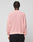 A person with short, twisted hair stands with their back to the camera, wearing a loose-fitting light pink LFDY Knit Sweater by LIVE FAST DIE YOUNG and black pants against a plain light gray background.