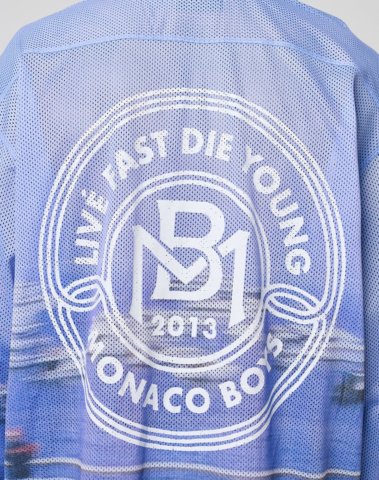 A close-up of the LFDY Yacht Jersey by LIVE FAST DIE YOUNG, a blue mesh oversized jacket with a white circular back logo reading LIVE FAST DIE YOUNG, MB1 2013, MONACO BOYS. Made from 100% polyester.