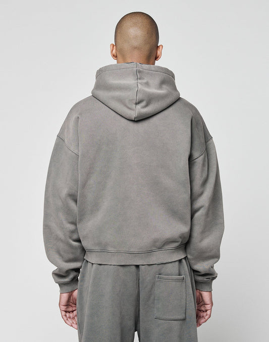 A person with a shaved head, seen from behind, wears a LIVE FAST DIE YOUNG Basic Hooded Zip in gray and matching subtly distressed pants. The background is plain and light-colored.