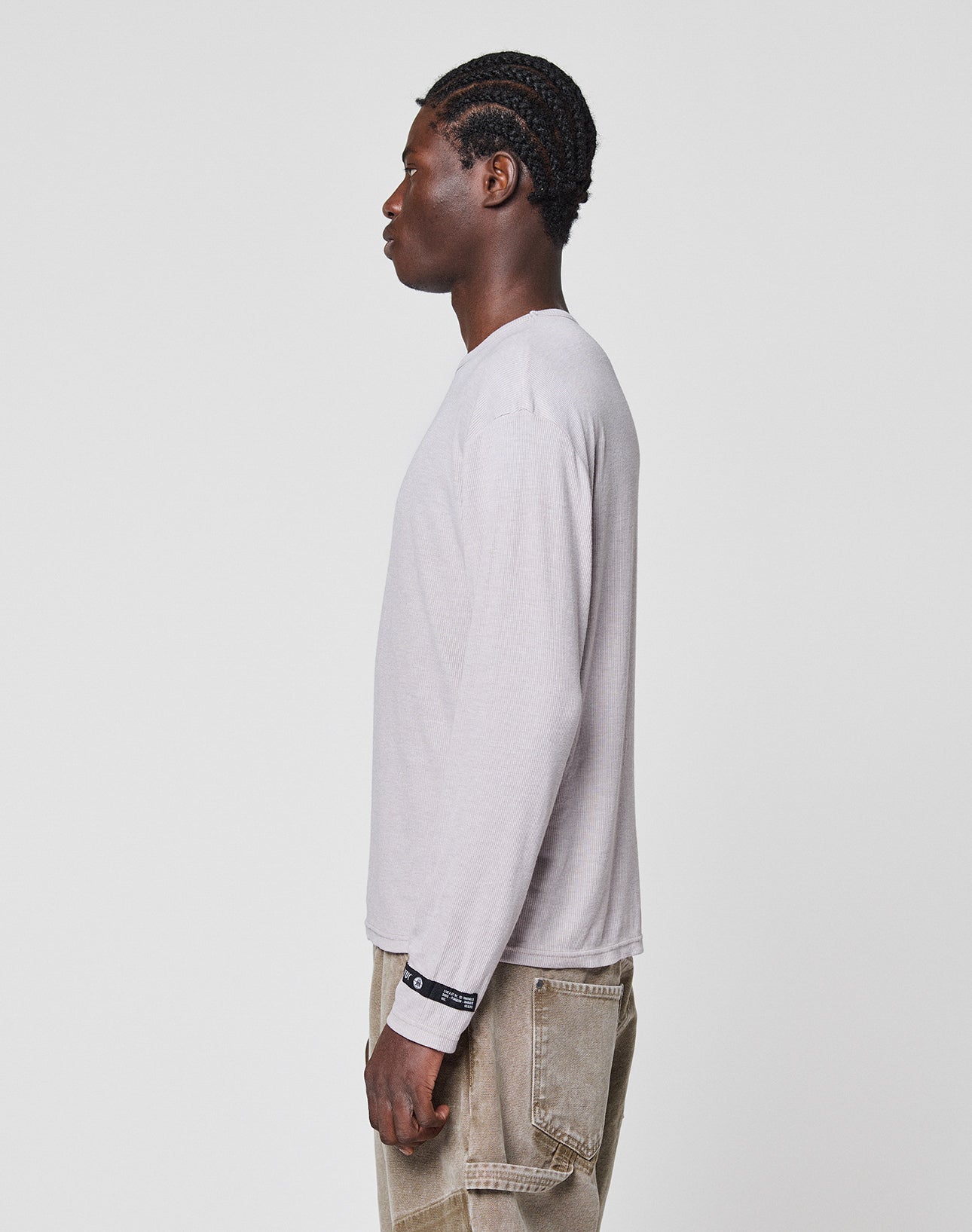 A person with braided hair stands in profile, facing left, wearing the LIVE FAST DIE YOUNG LFDY Rib Longsleeve in light gray and beige pants, set against a plain white background.