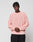 Wearing the LIVE FAST DIE YOUNG LFDY Knit Sweater in light pink with an oversized, ribbed design and paired with black pants, a person stands against a plain light gray background with hands clasped in front.