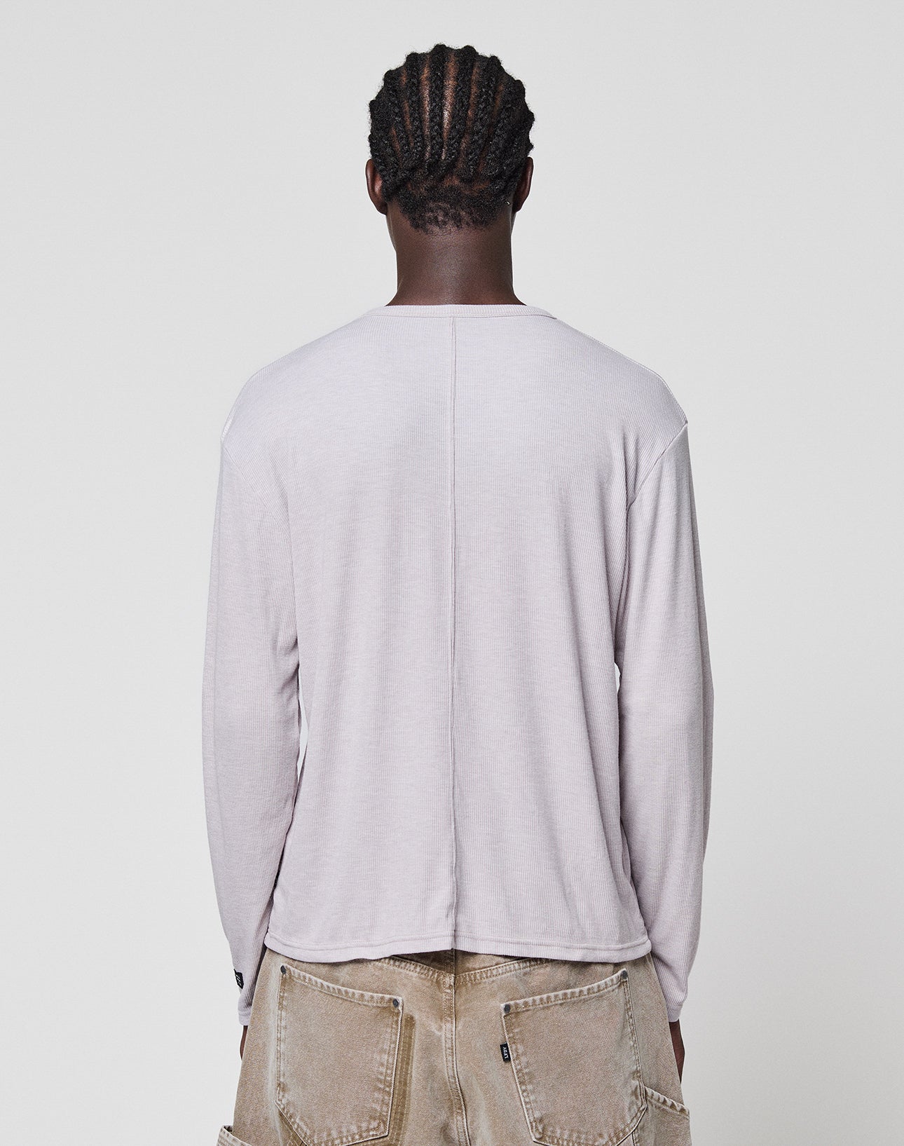 A person with cornrow braids, seen from behind against a white background, wears the LFDY Rib Longsleeve by LIVE FAST DIE YOUNG and beige pants with large back pockets and visible topstitching.