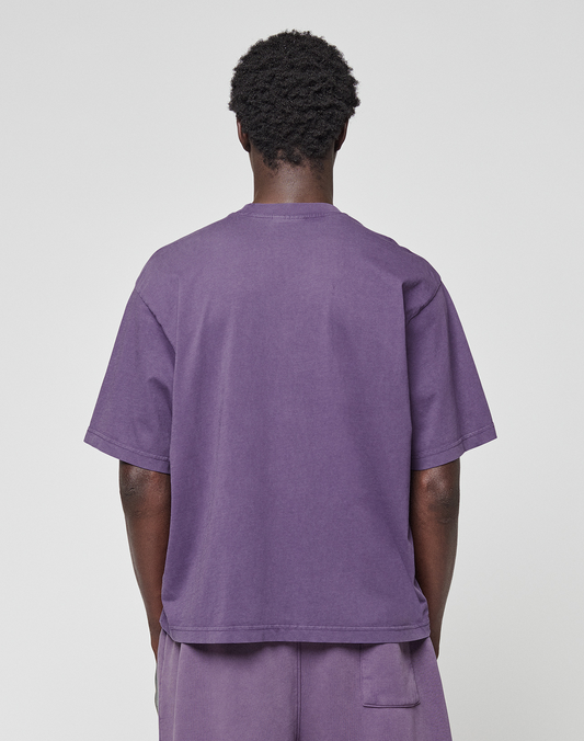 A person faces away from the camera, wearing the LIVE FAST DIE YOUNG Basic OS Livefast Tee and matching purple shorts, both in an oversize fit and made from 100% Baumwolle. The plain white background completes the look.