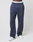 A person wears LIVE FAST DIE YOUNG LFDY Heavyweight Loungepants in dark blue (650gsm, wide fit), white sneakers, and a white waistband with "LIVE FAST" in black, standing against a plain white background. Cropped shoulders down.