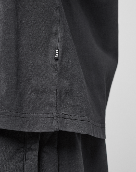 A close-up of the LFDY 40 Tee by LIVE FAST DIE YOUNG, featuring a small black AFRV tag on the seam. Crafted from soft, slightly textured 100% Baumwolle in an Oversize Fit, worn over matching black pants.