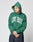 A person in the oversize fit green Live Fast College Hooded by LIVE FAST DIE YOUNG, with front print, stands against a plain light background, head down and hands clasped.