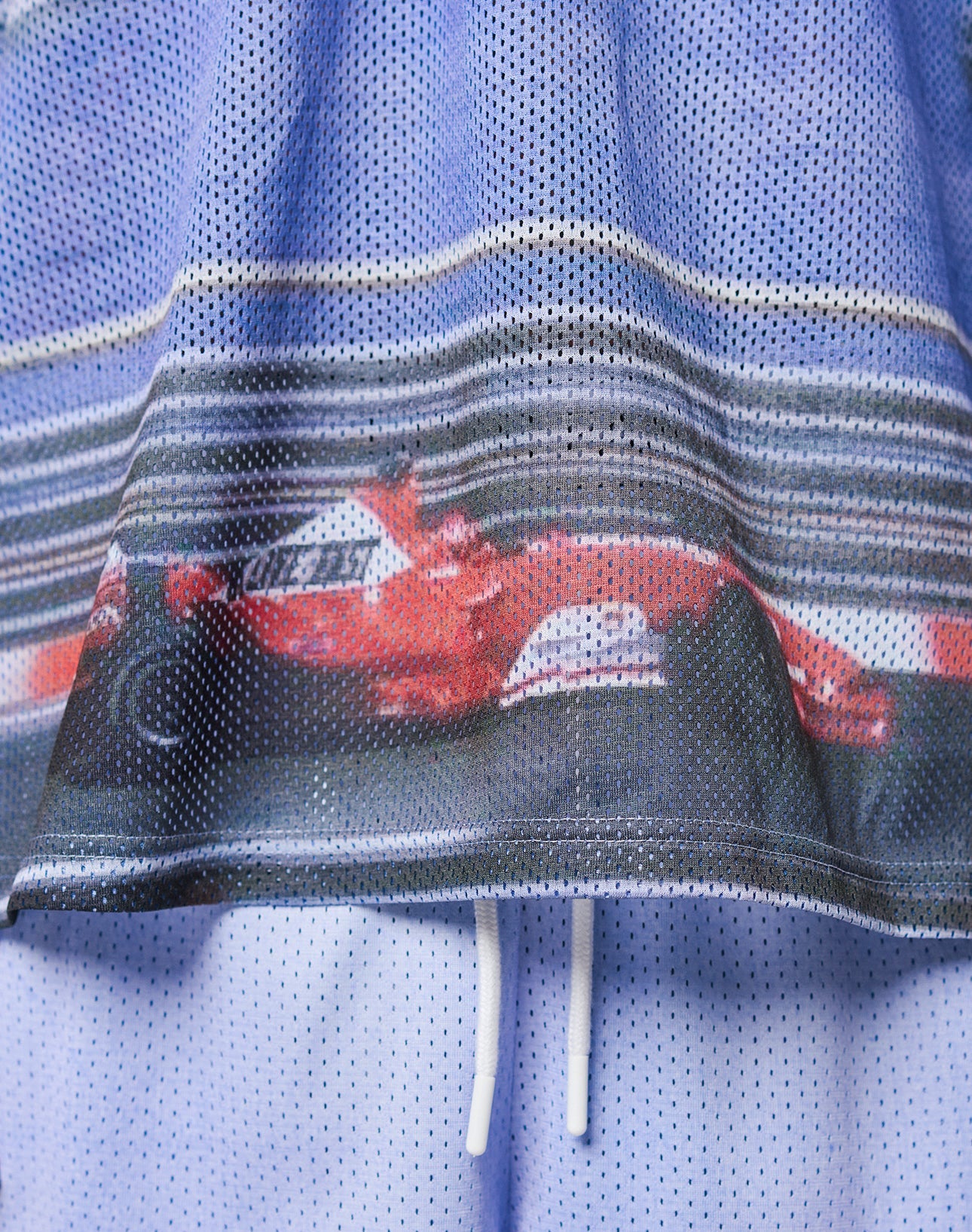 The LFDY Yacht Jersey by LIVE FAST DIE YOUNG is crafted from 100% polyester mesh and showcases a vivid red Formula 1 race car print with a blurred racetrack background, finished with white drawstrings.