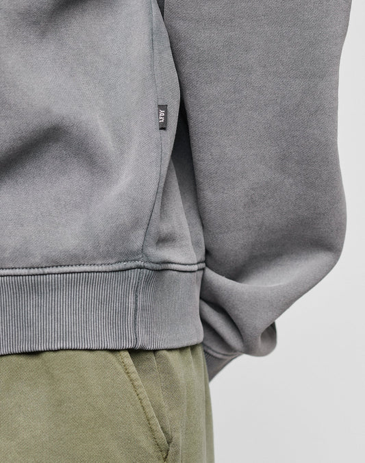 Close-up of a person wearing LIVE FAST DIE YOUNGs Basic Blank Sweater in light gray Oversize Fit, crafted from a Baumwolle-Polyester blend with ribbed hem and a small black and white tag near the side seam, paired with olive green pants.