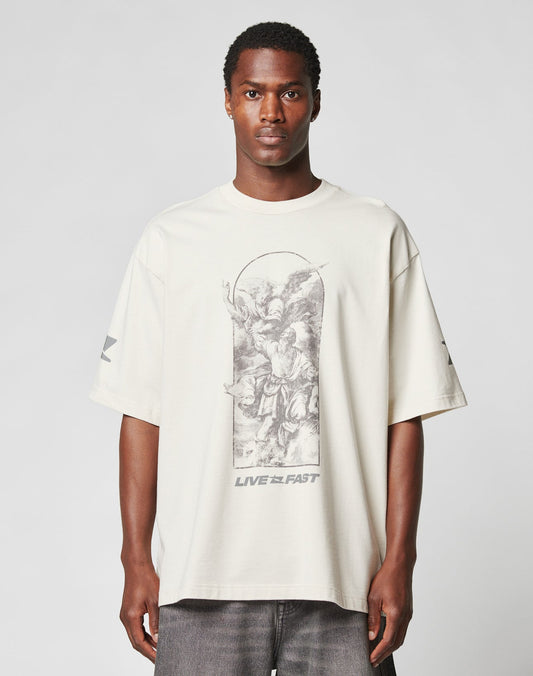 A man wears the LIVE FAST DIE YOUNG LFDY Window Tee, an oversize off-white 100% Baumwolle shirt with a black and white angel illustration, LIVE FAST text on the front, and reflective sleeve and logo prints, against a plain backdrop.