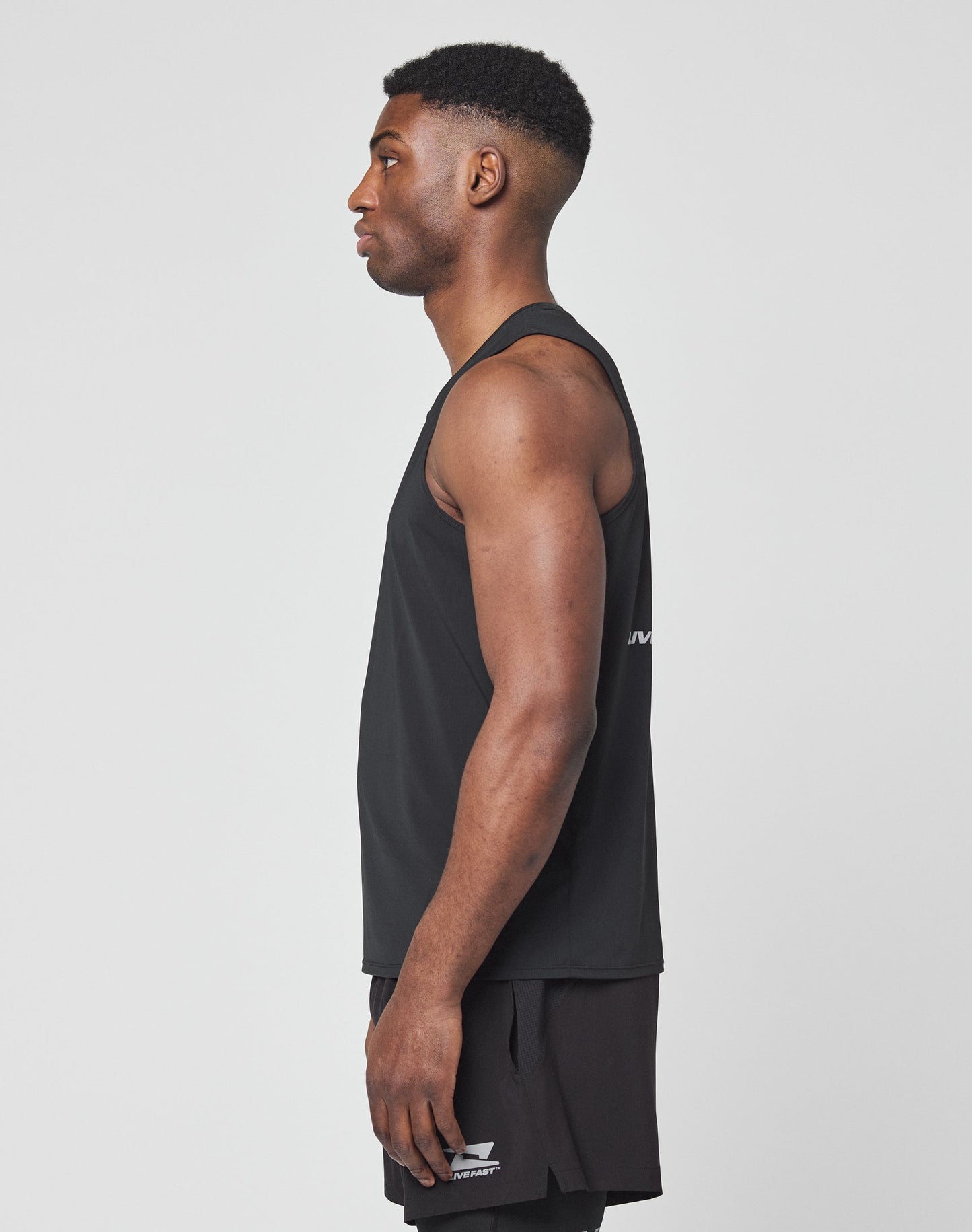 Close-up of a person wearing the black Live Fast Performance Tank by LIVE FAST DIE YOUNG, featuring a white logo and LIVE FAST in reflective print. Image shows only the neck and upper chest.