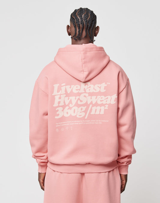 A person with braided hair, seen from behind, wears the LIVE FAST DIE YOUNG Basic 360 Hooded in pink—an oversized hoodie featuring large white text and additional small details on the back.