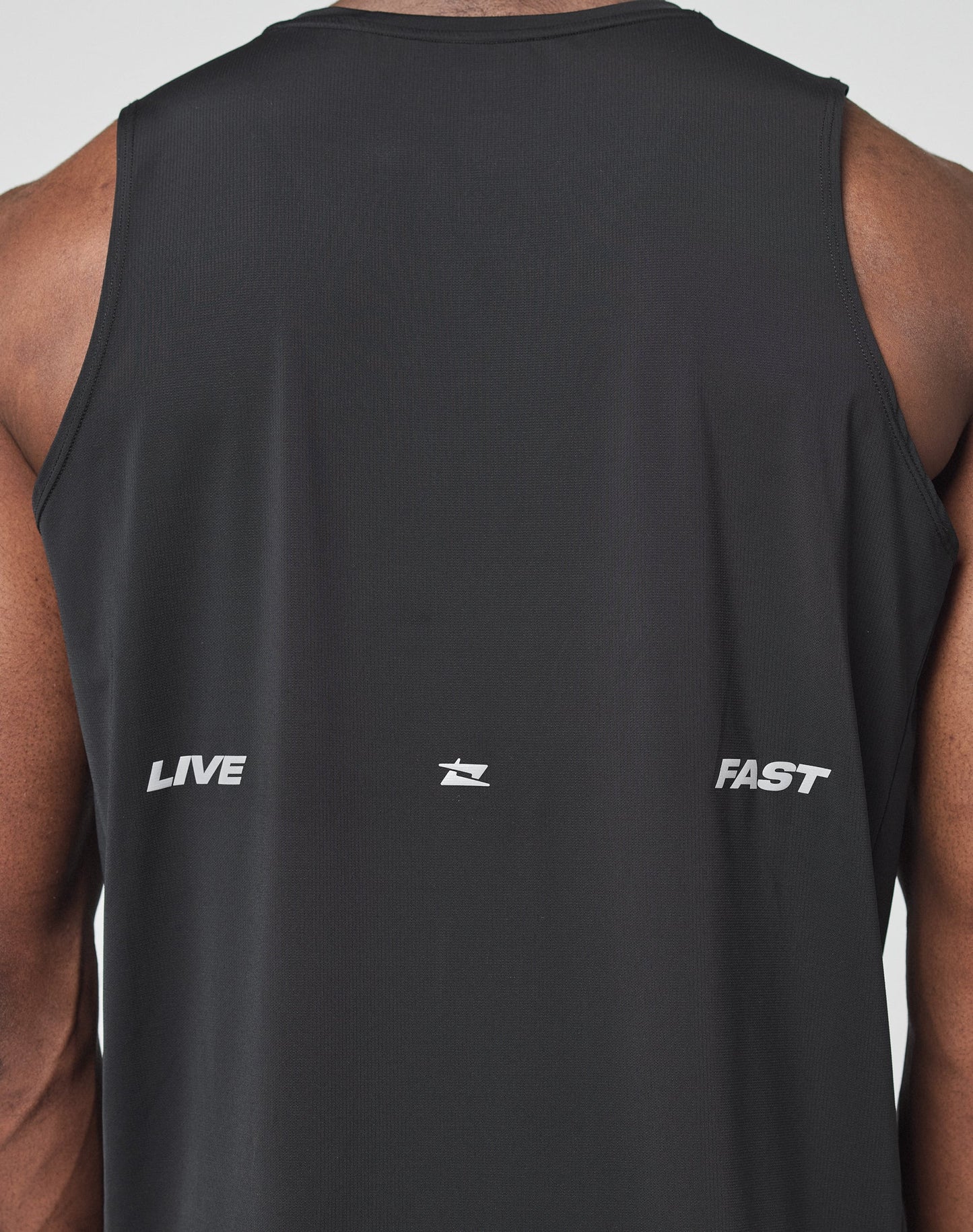 A man faces forward against a plain light background wearing the LIVE FAST DIE YOUNG Live Fast Performance Tank in slim fit black nylon spandex, paired with matching black shorts.| model