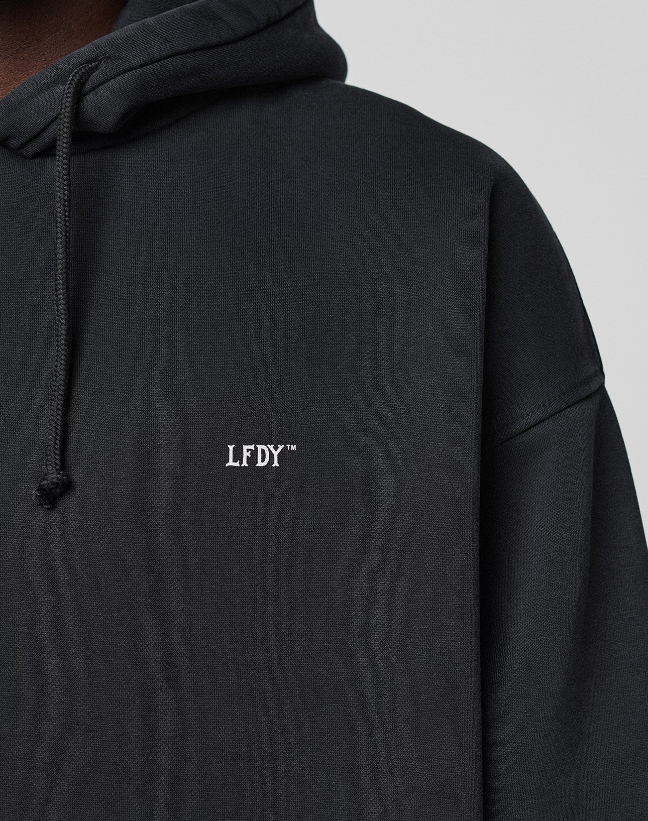 Close-up of the LIVE FAST DIE YOUNG Live Fast Vegas Hooded in black, an oversize fit hoodie with drawstring hood, small white LFDY™ chest embroidery, subtle front and back prints, and crafted from 65% Baumwolle.